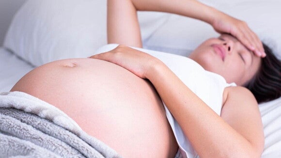 Mulher grávida deitada com os olhos fechados, com uma mão na barriga e a outra mão na cabeça. Mulher grávida deitada com os olhos fechados, com uma mão na barriga e a outra mão na cabeça.