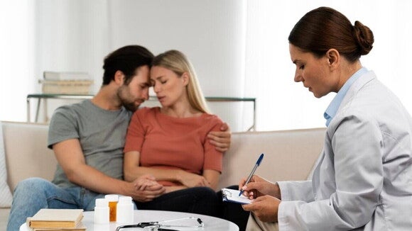 Uma profissional da saúde em uma clínica médica, fazendo uma anotação, enquanto falan com um casal preocupado sentado em um sofá. Uma profissional da saúde em uma clínica médica, fazendo uma anotação, enquanto falan com um casal preocupado sentado em um sofá.