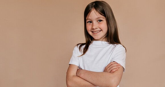 Menina de cabelo liso usando camiseta branca sorrindo com os braços cruzados Menina de cabelo liso usando camiseta branca sorrindo com os braços cruzados