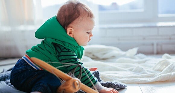 Bebê sentado no chão vestindo roupas de frio e aprendendo a engatinhar Bebê sentado no chão vestindo roupas de frio e aprendendo a engatinhar
