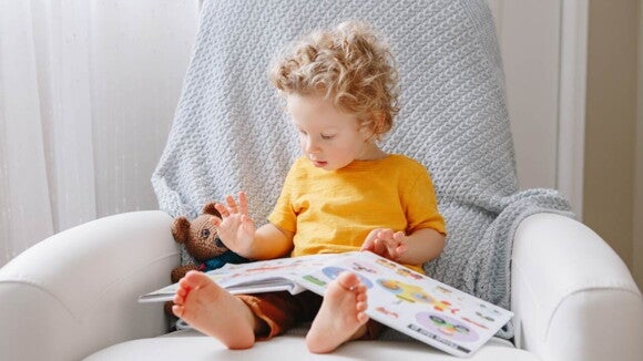 Uma criança está sentada em uma poltrona segurando um livro infantil. Uma criança está sentada em uma poltrona segurando um livro infantil.
