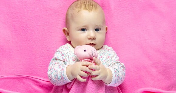 Bebê deitada na cama usando roupa cor de rosa e abraçando ursinho de pelúcia. Bebê deitada na cama usando roupa cor de rosa e abraçando ursinho de pelúcia.