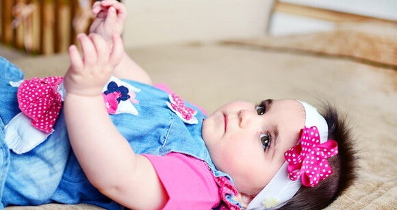 Bebê usando vestido jeans com flores cor de rosa e faixa na cabeça deitada de barriga para cima. Bebê usando vestido jeans com flores cor de rosa e faixa na cabeça deitada de barriga para cima.