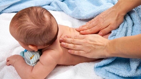 massagem shantala para bebê sendo aplicada nas costas, com o bebê deitado de bruços sobre uma toalha azul.
