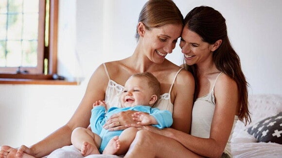 Duas mães sorrindo para seu bebê no colo. Duas mães sorrindo para seu bebê no colo.