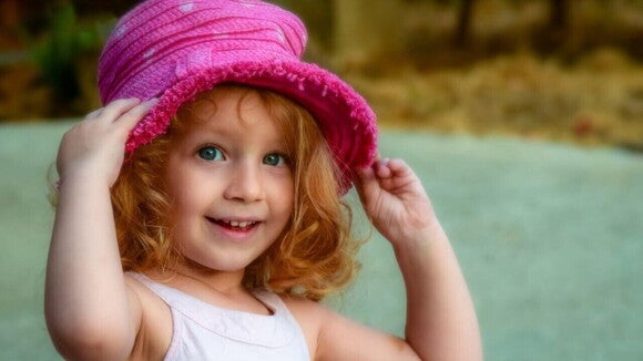 Menina sorrindo com as mãos em um chapéu rosa sobre a sua cabeça Menina sorrindo com as mãos em um chapéu rosa sobre a sua cabeça