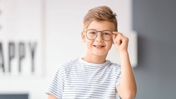 Menino com uma camiseta listrada, sorrindo e segurando a armação do óculos no rosto Menino com uma camiseta listrada, sorrindo e segurando a armação do óculos no rosto