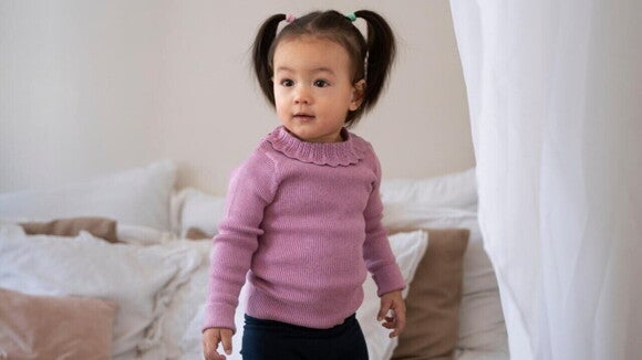 Uma menina de aproximadamente 2 anos, usando uma blusa lilás e calça preta, posando em um quarto. Uma menina de aproximadamente 2 anos, usando uma blusa lilás e calça preta, posando em um quarto.