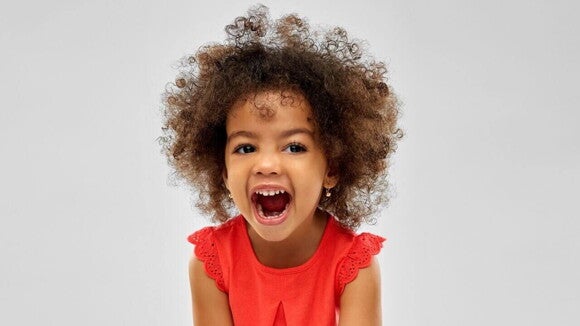 Menina sorridente de aproximadamente 4 anos de idade de cabelo crespo e roupa vermelha em um fundo claro. Menina sorridente de aproximadamente 4 anos de idade de cabelo crespo e roupa vermelha em um fundo claro.