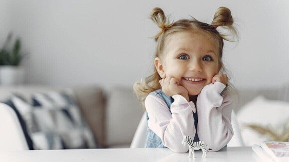 Menina sorrindo com os braços sobre a mesa apoiando o rosto Menina sorrindo com os braços sobre a mesa apoiando o rosto