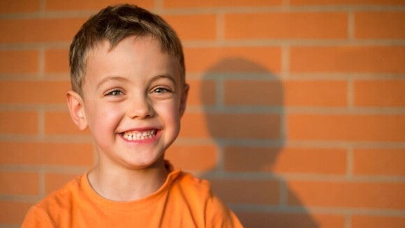 Menino vestindo uma camiseta laranja e sorrindo em frente a uma parede de tijolos Menino vestindo uma camiseta laranja e sorrindo em frente a uma parede de tijolos