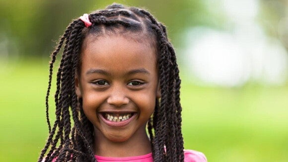 Menina com tranças e blusa rosa sorrindo e olhando diretamente para a câmera. Menina com tranças e blusa rosa sorrindo e olhando diretamente para a câmera.