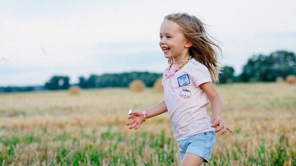 Menina sorridente de blusa cor de rosa e short jeans correndo em um campo verde. Menina sorridente de blusa cor de rosa e short jeans correndo em um campo verde.