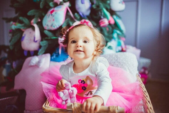 Bebê menina sorrindo enquanto brinca em um cesto perto de uma árvore de Natal decorada. Bebê menina sorrindo enquanto brinca em um cesto perto de uma árvore de Natal decorada.
