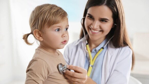 Uma pediatra sorrindo e utilizando um estetoscópio para examinar uma criança. Uma pediatra sorrindo e utilizando um estetoscópio para examinar uma criança.