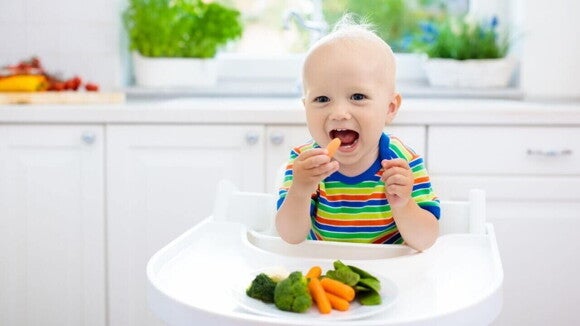 Bebê sorrindo, sentado em uma cadeira, comendo vegetais diversos Bebê sorrindo, sentado em uma cadeira, comendo vegetais diversos