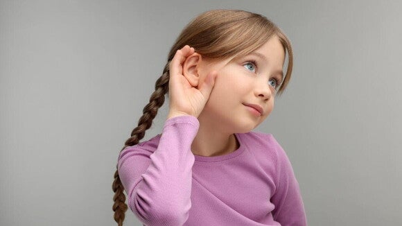Uma menina com a mão em forma de concha em volta da orelha Uma menina com a mão em forma de concha em volta da orelha