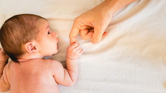 Um recém-nascido, deitado, segura o dedo de um adulto. A imagem representa o vínculo entre pais e bebê, e pode ser usada para ilustrar a importância do cuidado e acompanhamento para evitar a perda de peso neonatal excessiva.