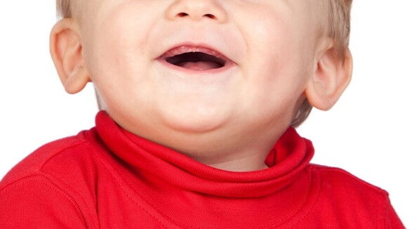 Close de um bebê sorridente, vestindo uma roupa vermelha, com uma expressão alegre deixando a gengiva à mostra. Close de um bebê sorridente, vestindo uma roupa vermelha, com uma expressão alegre deixando a gengiva à mostra.
