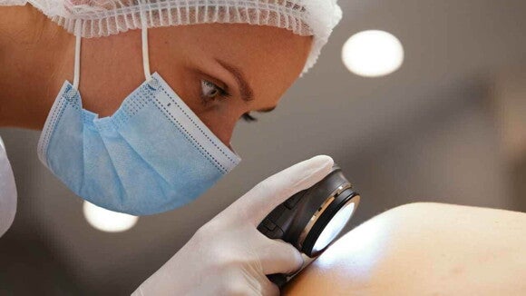 Profissional da saúde observando de perto a pele de um paciente utilizando um aparelho luminoso. Profissional da saúde observando de perto a pele de um paciente utilizando um aparelho luminoso.