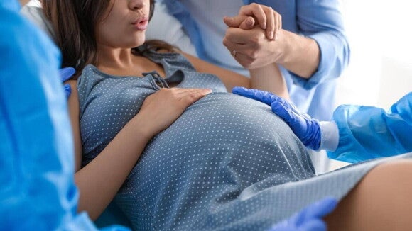 Mulher grávida fazendo exercício de respiração com a mão na barriga, sendo amparada por profissionais da saúde. Mulher grávida fazendo exercício de respiração com a mão na barriga, sendo amparada por profissionais da saúde.