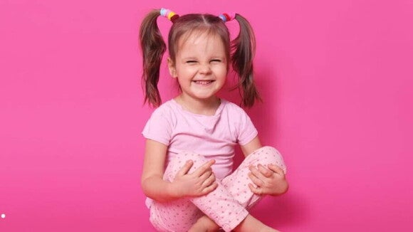 Menina sorridente usando blusa e calça cor de rosa sentada com as pernas cruzadas e mãos nos joelhos. Menina sorridente usando blusa e calça cor de rosa sentada com as pernas cruzadas e mãos nos joelhos.