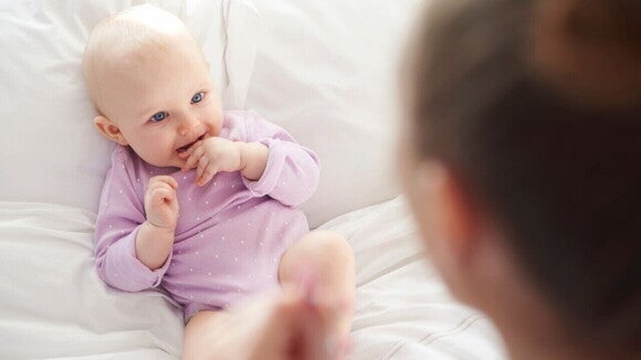Um bebê deitado em uma cama branca, sorrindo e olhando para a mãe, representando a fase quando o bebê começa a enxergar e reconhecer as pessoas próximas. Um bebê deitado em uma cama branca, sorrindo e olhando para a mãe, representando a fase quando o bebê começa a enxergar e reconhecer as pessoas próximas.