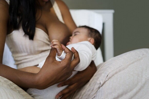 Mãe sentada, amamentando um bebê em seu colo e segurando a mão dele Mãe sentada, amamentando um bebê em seu colo e segurando a mão dele