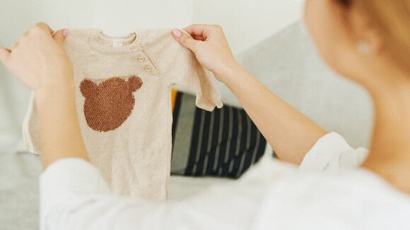 Uma mulher segurando uma roupa de bebê rosa com o desenho de um urso. Uma mulher segurando uma roupa de bebê rosa com o desenho de um urso.