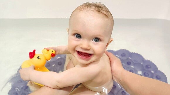 Bebê sorrindo alegremente durante o banho enquanto segura um patinho de borracha.