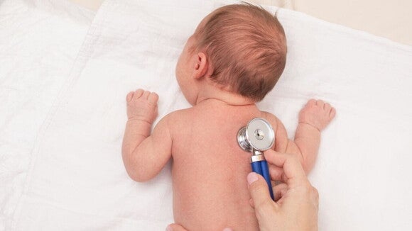 Um bebê deitado de costas sendo examinado por um estetoscópio