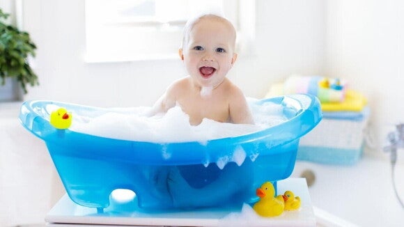 Bebê em uma banheira infantil cheia de espuma, com patos de borracha à sua volta. Bebê em uma banheira infantil cheia de espuma, com patos de borracha à sua volta.