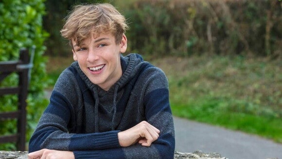 Um jovem sorrindo, sentado em uma mesa ao ar livre, vestindo uma roupa de frio. Um jovem sorrindo, sentado em uma mesa ao ar livre, vestindo uma roupa de frio.