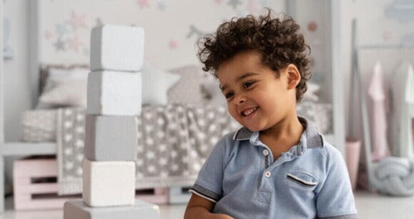 Criança sorrindo enquanto brinca com blocos empilhados, usando uma camisa azul em um ambiente infantil decorado. Criança sorrindo enquanto brinca com blocos empilhados, usando uma camisa azul em um ambiente infantil decorado.