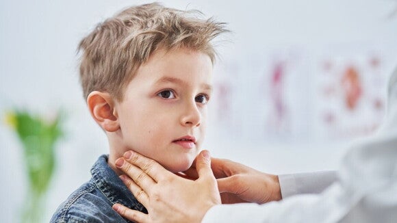 Um menino olha para o lado enquanto um médico toca suavemente seu pescoço e mandíbula. Um menino olha para o lado enquanto um médico toca suavemente seu pescoço e mandíbula.