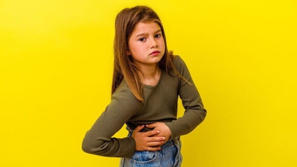 Uma menina em um fundo amarelo, com expressão de dor, segurando a região abdominal, sugerindo desconforto. Uma menina em um fundo amarelo, com expressão de dor, segurando a região abdominal, sugerindo desconforto.