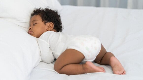 Bebê dormindo deitado de bruços em uma cama. Bebê dormindo deitado de bruços em uma cama.