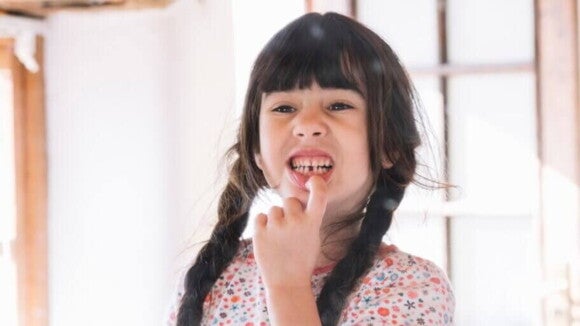 Menina apontando para um espaço vazio entre os seus dentes Menina apontando para um espaço vazio entre os seus dentes