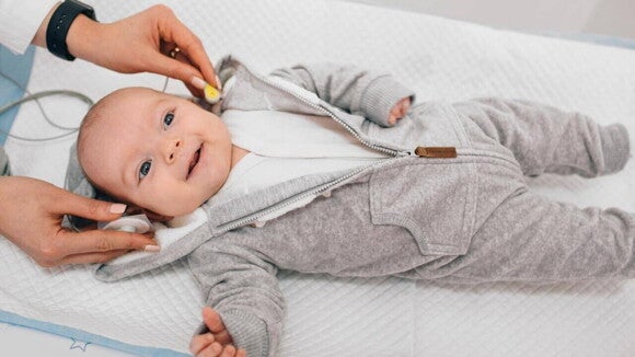 Bebê deitado sorrindo durante a realização do teste da orelhinha, exame essencial para avaliar a audição nos primeiros dias de vida.
