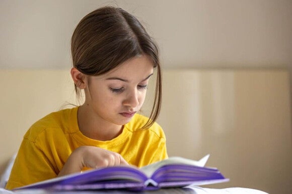 Uma menina sentada e com feição de concentração, lendo um livro. Uma menina sentada e com feição de concentração, lendo um livro.