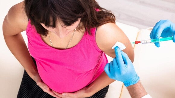 Gestante recebendo a vacina da coqueluche no braço esquerdo por profissional de saúde com luvas azuis