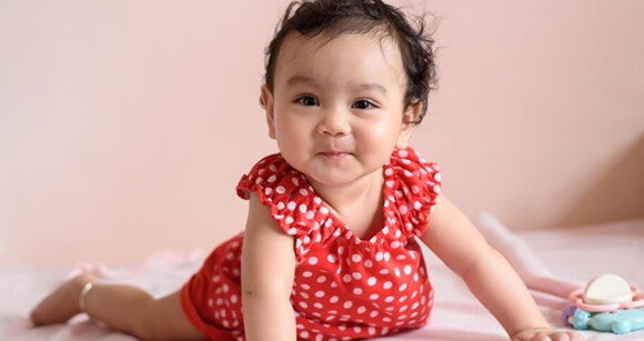 Bebê usando vestido vermelho de bolinhas brancas engatinhando no chão. Bebê usando vestido vermelho de bolinhas brancas engatinhando no chão.